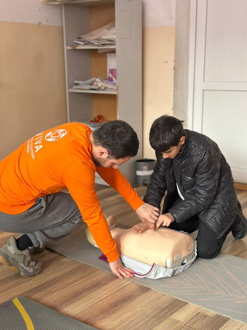 VIVA Foundation instructor in an orange shirt coaching a student through CPR practice in Armenia